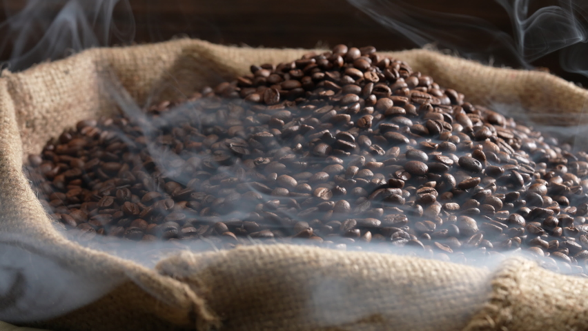 Hand holding a ladle scooping up roasted coffee beans from a pile of beans in burlap sack with cloud of smoke on top. Slow motion. Royalty-Free Stock Footage #1089203811