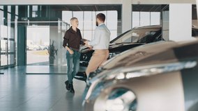 Customers looking at cars in showroom. Cool design. Handsome young bearded man and woman buys and inspects a crossover car in a dealership. Male car seller with blond female customer in car salon. - Powered by Shutterstock - Get 15% off with code: PIKWIZARD15