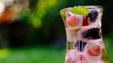 Berry cocktail.Splashes and drops of a Summer drink.Cocktail with gooseberries and blackberries, mint and ice cubes in a glass transparent glass in a summer garden in the sun.Berry drink with ice 