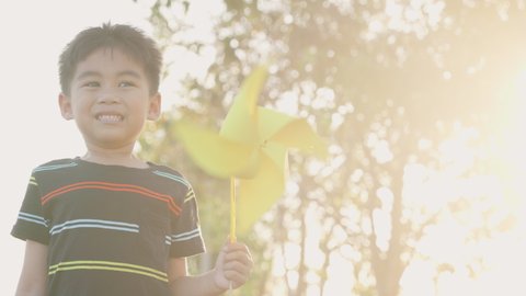 Asian child boy playing with pinwheels, Happiness little boy smiling in wheat field holding small wind wheel or windmill toy on hand in summer day in the park garden