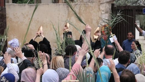 Jerusalem, Israel Apr 10, 2022: Joyful priests pour holy water onto Christians crowd with palm tree leaves on street at Palm Sunday. Entry of Our Lord into Jerusalem tradition