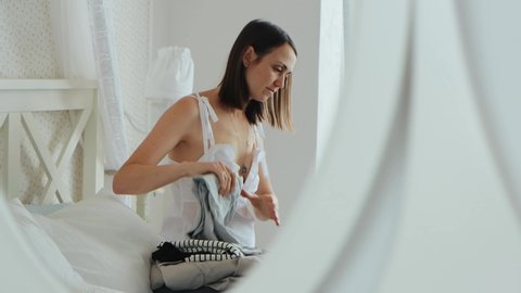 Young woman in white sleepwear is packing the blue plastic suitcase in hotel interior. View through the reflection in the mirror, 4k