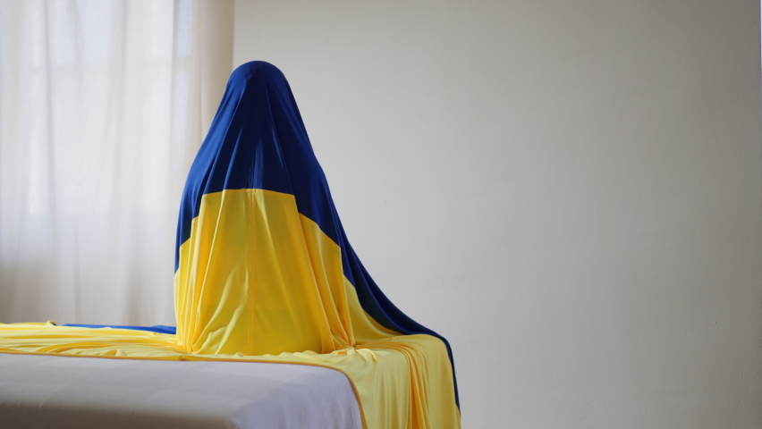 Unrecognizable person sitting, covered with Ukrainian flag, unity with Ukraine concept.
