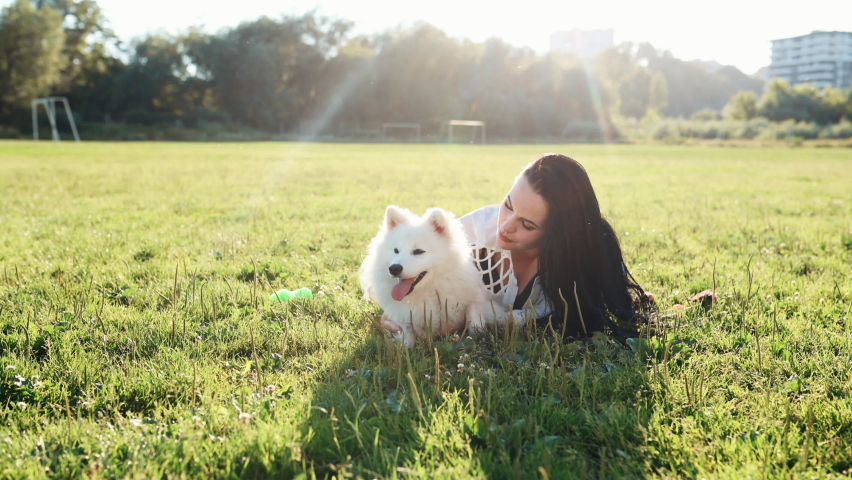 Brunette having a walk with her white dog outdoors on the field at daytime.