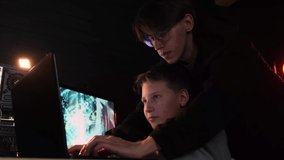 Two boys  looking computer screen and play game online together. Neon led lightning is in room. Dark evening. 