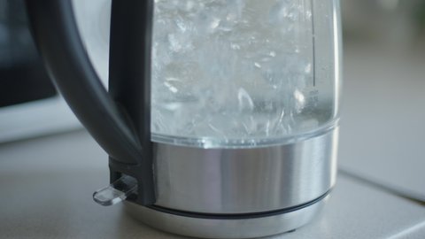 Electric kettle turning off automatically as water boiling inside close-up. Domestic kitchenware appliance on table indoors