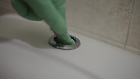 Female finger in rubber gloves pushing push button on toilet flush tank close-up. Unrecognizable housewife cleaning bathroom with chemical detergents at home indoors. Purity and hygiene concept