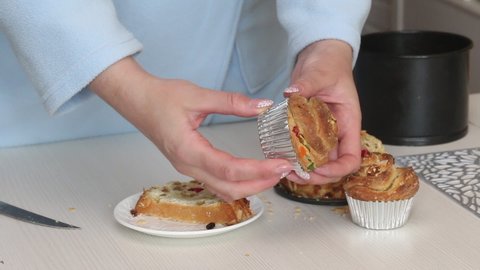 A woman demonstrates a cooked cruffin with raisins and candied fruit. Medium plan.