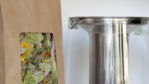tea pack, brown kraft recycled paper with window, natural  leaves, harvest from garden and glass kettle. woman takes natural tea leaves from pack and putt in kettle, borosilicate glass.