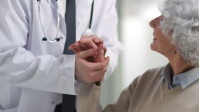 Cropped shot of doctor in white coat holding hand of senior patient. Elderly smiling woman looking up at medical specialist talking about rehabilitation - Powered by Shutterstock - Get 15% off with code: PIKWIZARD15