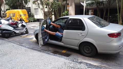 Tired car driver, sleeping in the car with his feet over the door. Lazy man wearing blue shoes, sleeping on the road waiting, shaking his foot. Gray Fiat Siena car. Rio de Janeiro, Brazil. 04.08.22