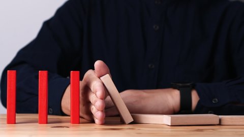 Businessman hand stopping continuous failing domino wooden effect. Concept of Risk Management, Business Crisis, Domino Effect, Investment, Finance, Risk, Disaster, Protection, Prevention, Opportunity