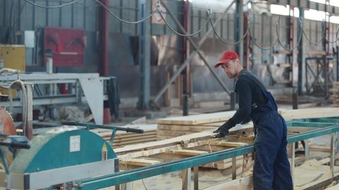 Worker is placing a long timber board into the machine on a production line. Worker is lining up the timber board with the machine. Worker is stacking two timber boards together before processing.