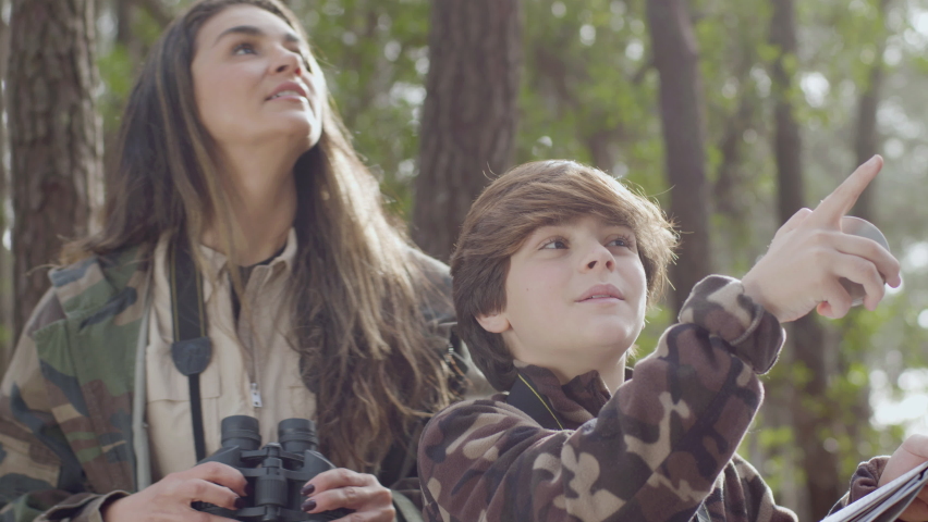 Young woman helping her son with biology project while hiking together in natural park and watching birds. Boy holding map and compass while mum looking through binoculars. Nature, education concept | Shutterstock HD Video #1089226671