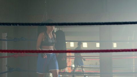 Beautiful slim girl jumping rope in boxing ring while warming up before training in boxing gym. Female boxer with bandages on fists exercising before doing sports. Sport, exercising concept