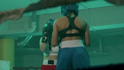 Two female boxers in helmets and boxing gloves fighting in ring at gym. Young sportswoman hitting sparring partner, knocking her out. Sport, boxing concept