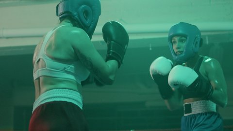 Two female boxers in helmets and boxing gloves fighting in ring at gym. Young sportswoman hitting sparring partner and knocking her out, then jumping with joy. Sport, boxing concept