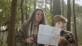 Excited mother and son exploring wildlife in natural park. Smart boy holding map and compass and pointing, then lady looking through binoculars, searching for rare species. Nature, discovery concept - Powered by Shutterstock - Get 15% off with code: PIKWIZARD15