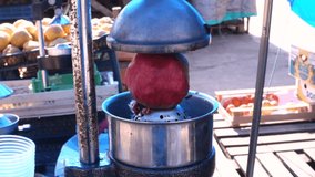 Apparatus for squeezing pomegranate juice. A man in the market is squeezing juice from a large ripe red pomegranate into a container.