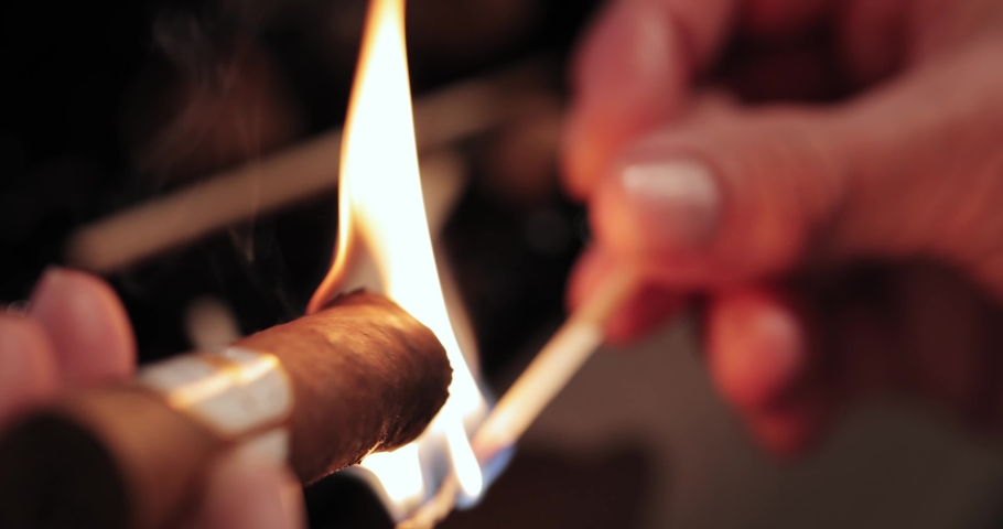 Men's hands hold a burning match and set fire to a Cuban cigar. view from above. macro | Shutterstock HD Video #1089230997