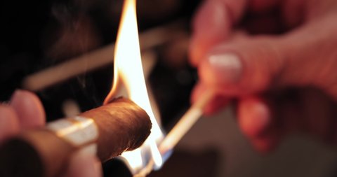 men's hands hold a burning match and set fire to a Cuban cigar. view from above. macro