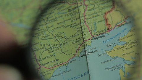 War in Ukraine. Look at map with magnifying glass close up near Mariupol, Berdyansk, Taganrog, Donetsk, Melitopol. Ukrainian language paper map