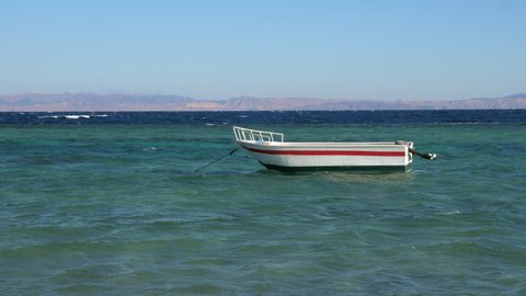 Empty white motorboat is rocking on Red sea waves. Fishing boat swaying on ripple water surface in windy day. Motor ship, outboard runabout floating near seaside. Travel, tourism, fishery
