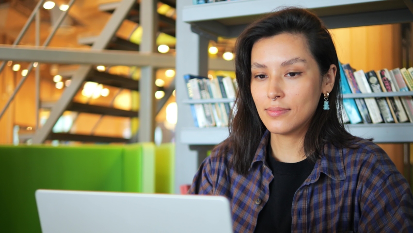 Attractive young woman looking at laptop screen at the library. Concept of office work, co-working, freelance, online learning. High quality 4K slowmotion portrait.