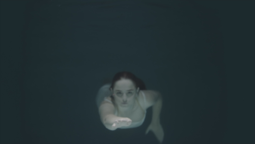 beautiful red-haired girl stopped underwater in front of the camera and froze