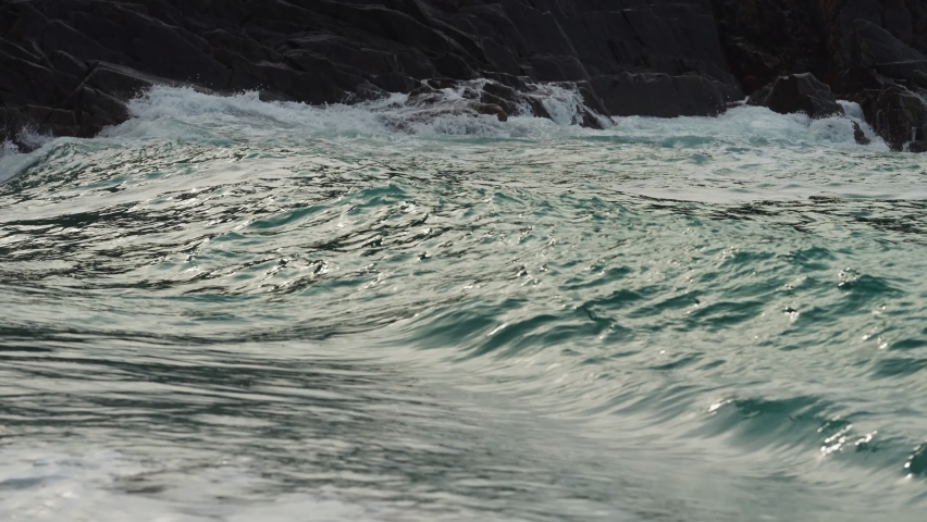 A close-up shot of the long low waves spilling on the sandy shore. Slow-motion.