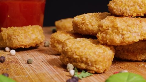 Close up of vegan chicken nuggets on a cutting board with some basil leaf and peppercorn garnish rotate against a black background