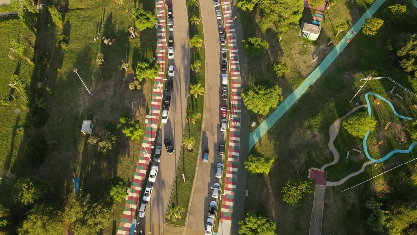 Aerial forward tilt up reveal over cars parked along road close to Kempes park at sunset. Cordoba city in Argentina