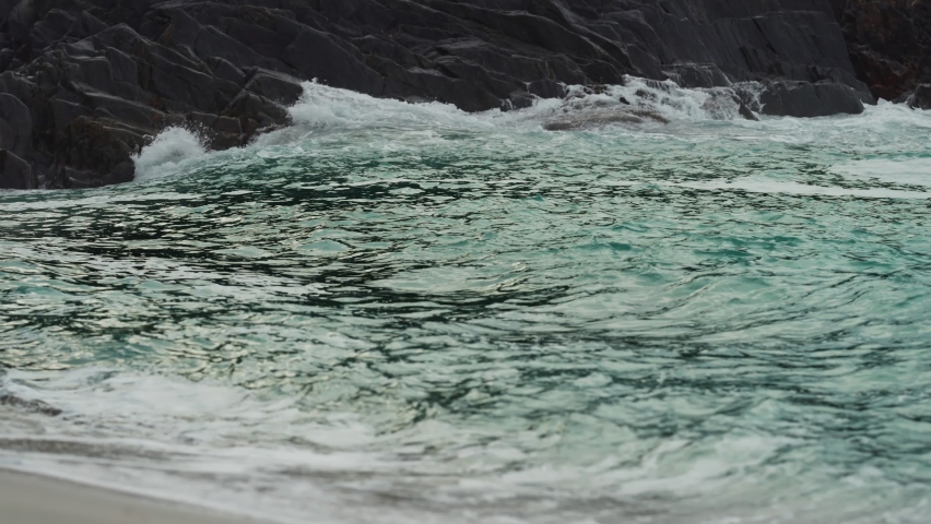 Strong waves are crashing on the rocky shore. Water spray rising in the air. Slow-motion, close-up shot.