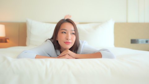 Close-up, an attractive woman lies on her stomach at the foot of a large bed while leaning her chin on her arms.