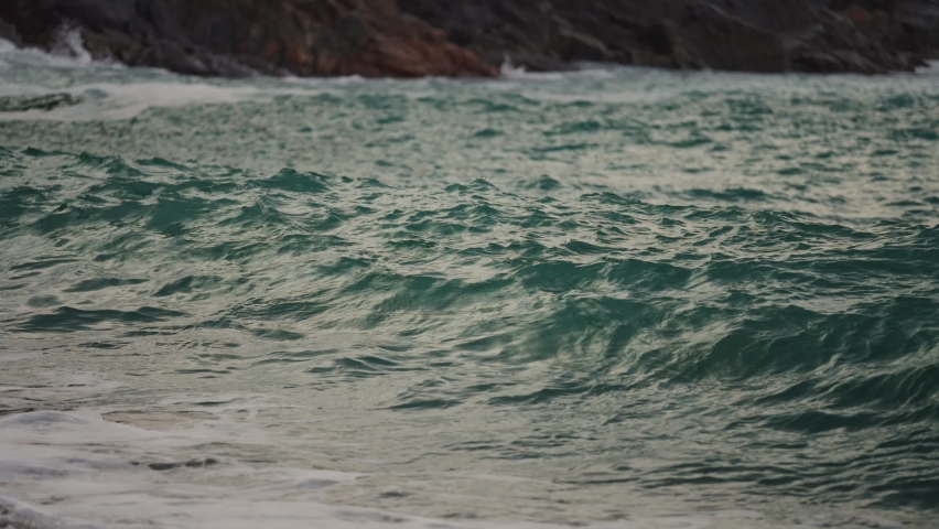 Powerful waves are crashing and spilling on the sandy beach. Slow-motion, close-up shot.