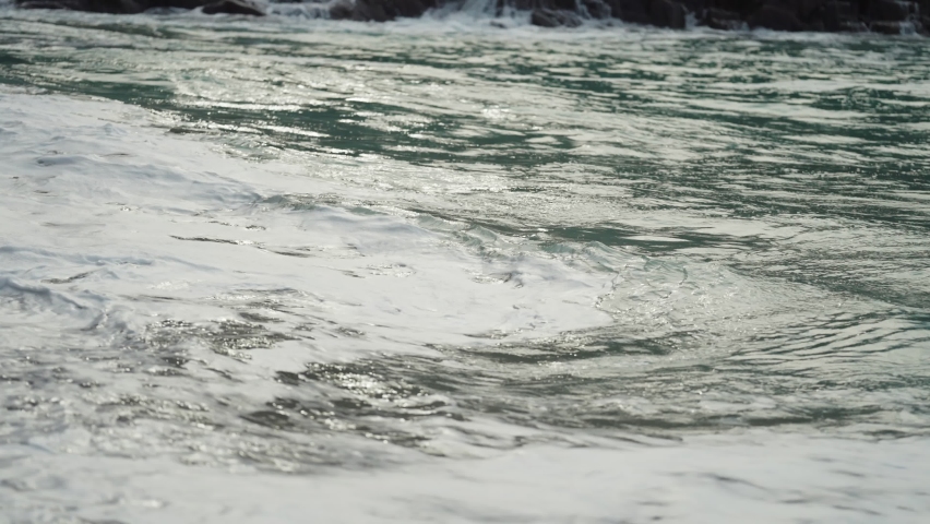 A close-up shot of the long waves spilling on the sandy beach. Slow-motion.