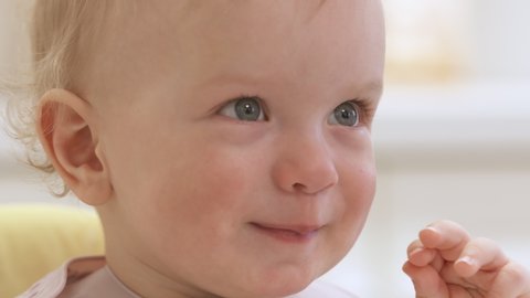 Happy kid face after feeding, one year old baby boy sitting in highchair at home, child smiling close-up. High quality 4k footage