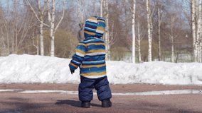 Kid takes first steps in the snow in winter, 1 year old baby boy learning to walk in the park. High quality 4k footage