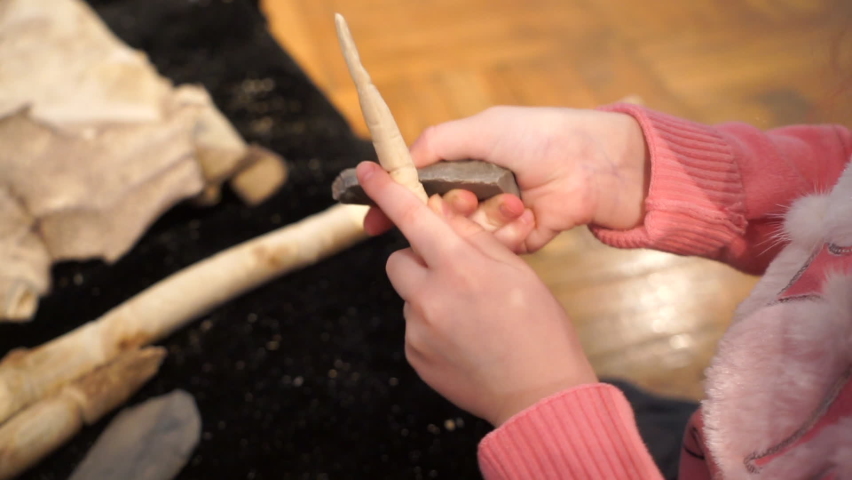 Person learns to sharpen a wooden tip on the skin of an animal indoors
