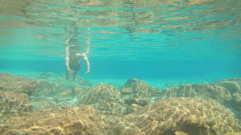 young man swimming in blue clear under water of waterfall with many rocks from flat angle