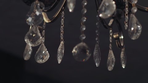 Shiny transparent drop shaped crystal ornate on vintage chandelier in semi-dark room closeup. Home decor classic element. Design ideas for interior