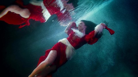 happy carefree brunette woman in red suit of Santa is floating underwater, amazing Xmas fairytale