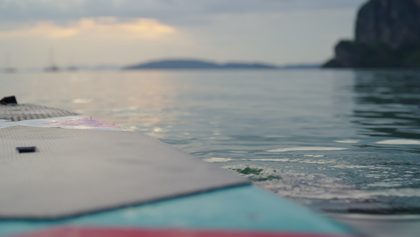 4K Confidence young Asian man swimming in sea water and paddleboarding passing beautiful sea at summer sunset. Healthy strong male enjoy outdoor active lifestyle and water sports on holiday vacation