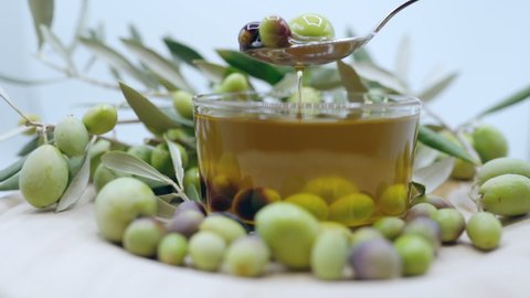 Production of organic olive oil from natural olive fruits grown on field plantations, healthy natural product on white background, spoon with ripe olive fruits and dropping oil into transparent bowl