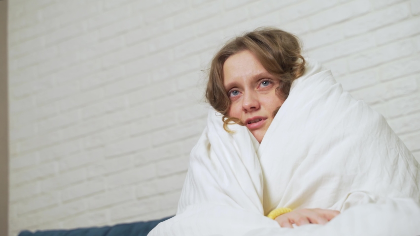 Symptoms of flu. A sick young woman, feeling cold fever, freezes without central heating, feeling cold at home. Covered with a warm white blanket. Shivering, sitting on the couch, stressed out Royalty-Free Stock Footage #1089249899