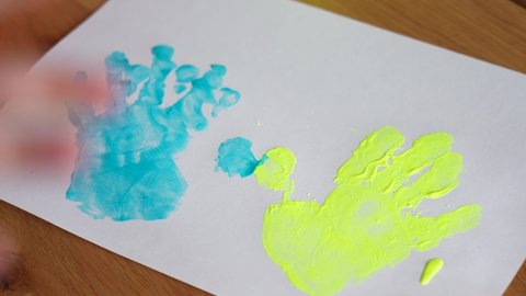 Close-up view 4k stock video footage of small hands of 4 or 5 years old baby painted in bright blue and yellow colors of national Ukrainian flag. Baby making cute handprints on white paper sheet