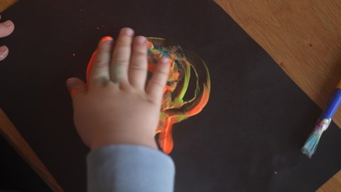 Closeup top view 4k stock video footage of cute small hand of little baby. Little child's fingers messing different bright paints on black  paper. Finger painting and drawing. Early development, art