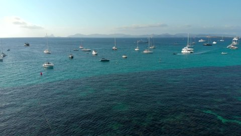 Drone video of Ses Illetes island in Formentera, surrounded by yatchs in crystal clear water