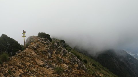 4k Static shot of fog and clouds around a mountain ridge with a hiking sign. La Concha mountain.