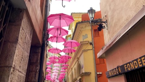 Grasse, France, October 3, 2021: SLOW MO Suspended pink umbrellas in the historic center of Grasse, celebrating the Rose Expo. Elements of architecture of Grasse with colored umbrellas between houses.